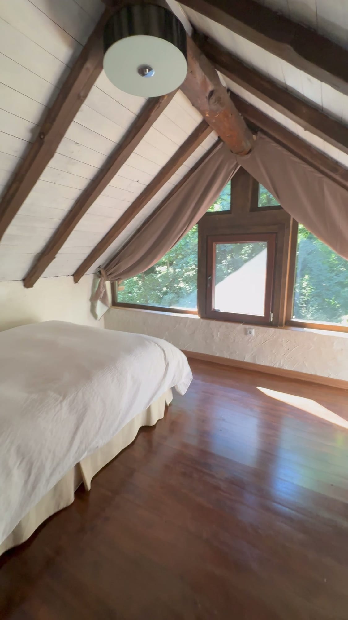 Dormitorio abuhardillado con cama blanca y vigas de madera en Cabañas Crisol