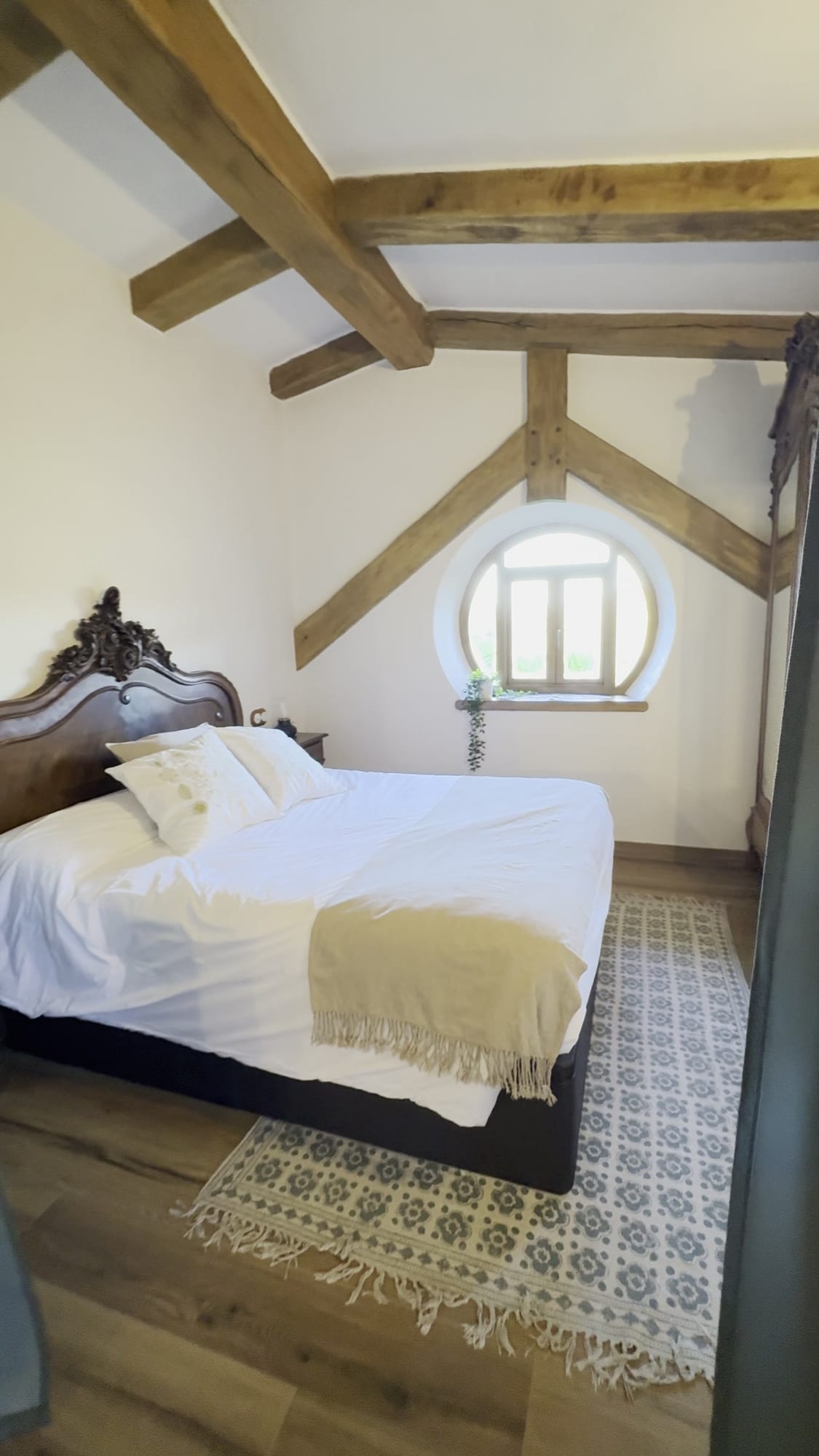 Dormitorio de la casita de La Comarca de Veratton con ventana redonda y vigas de madera