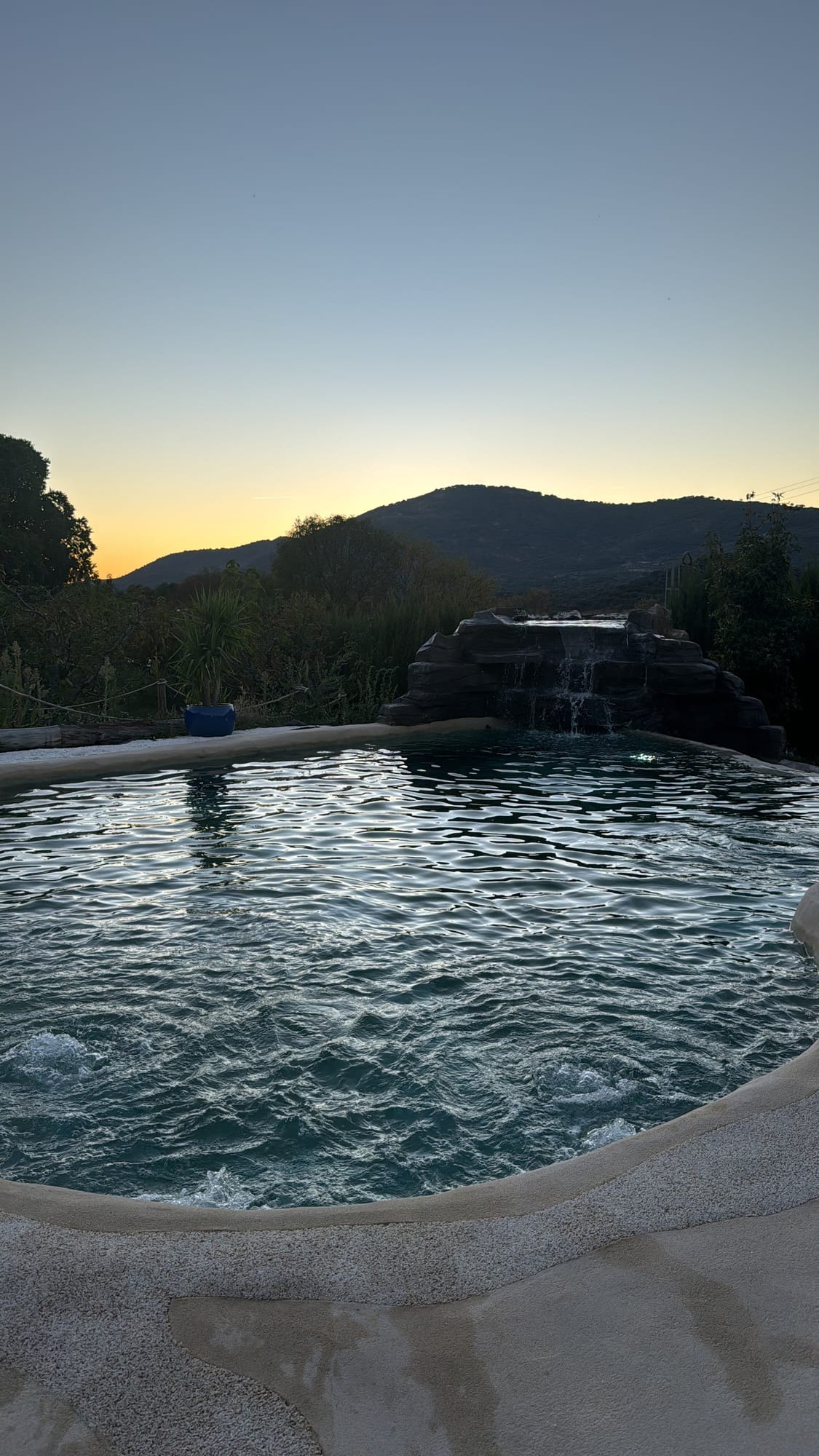 Piscina con cascada y la sierra al atardecer en El Jardín de las Delizias
