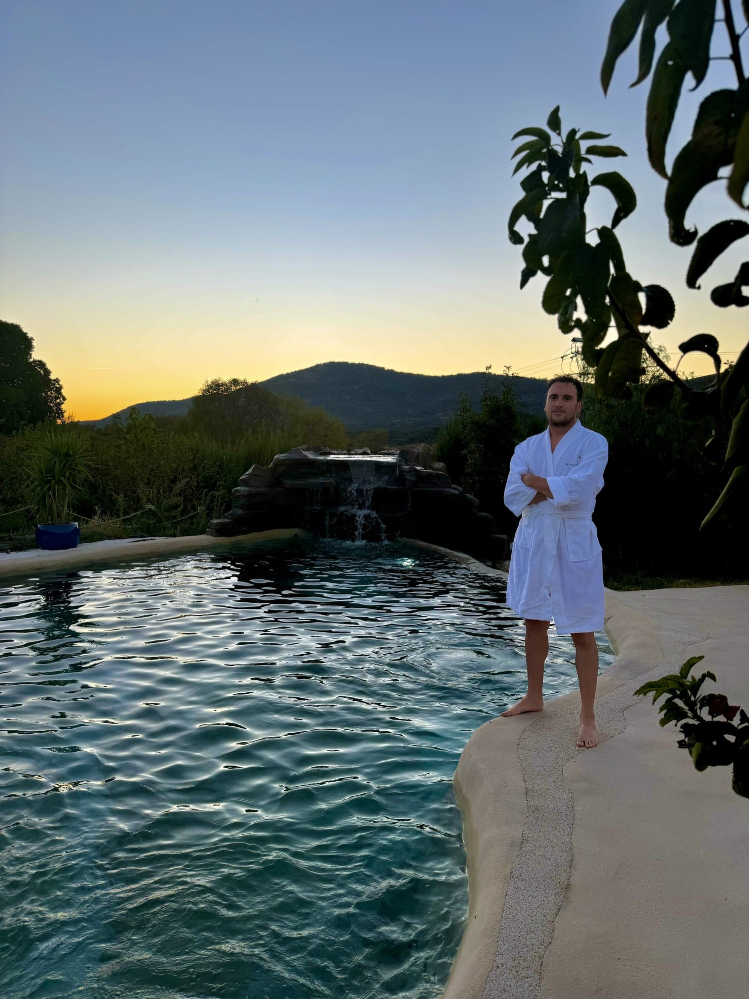 Javier Sobrino en albornoz junto a la piscina con cascada al atardecer en El Jardín de las Delizias