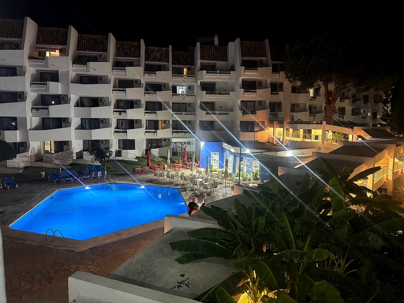 La piscina del Eurhostal iluminada de noche, con los bloques de apartamentos detrás