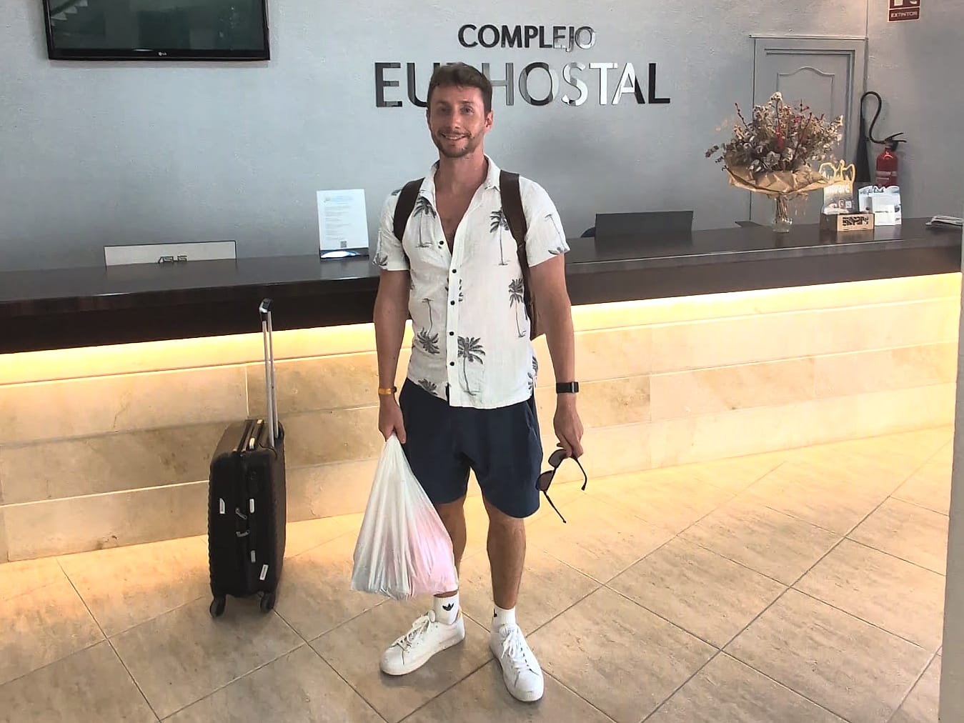 Javier Sobrino en la recepción del Eurhostal, con la maleta y el letrero del complejo detrás