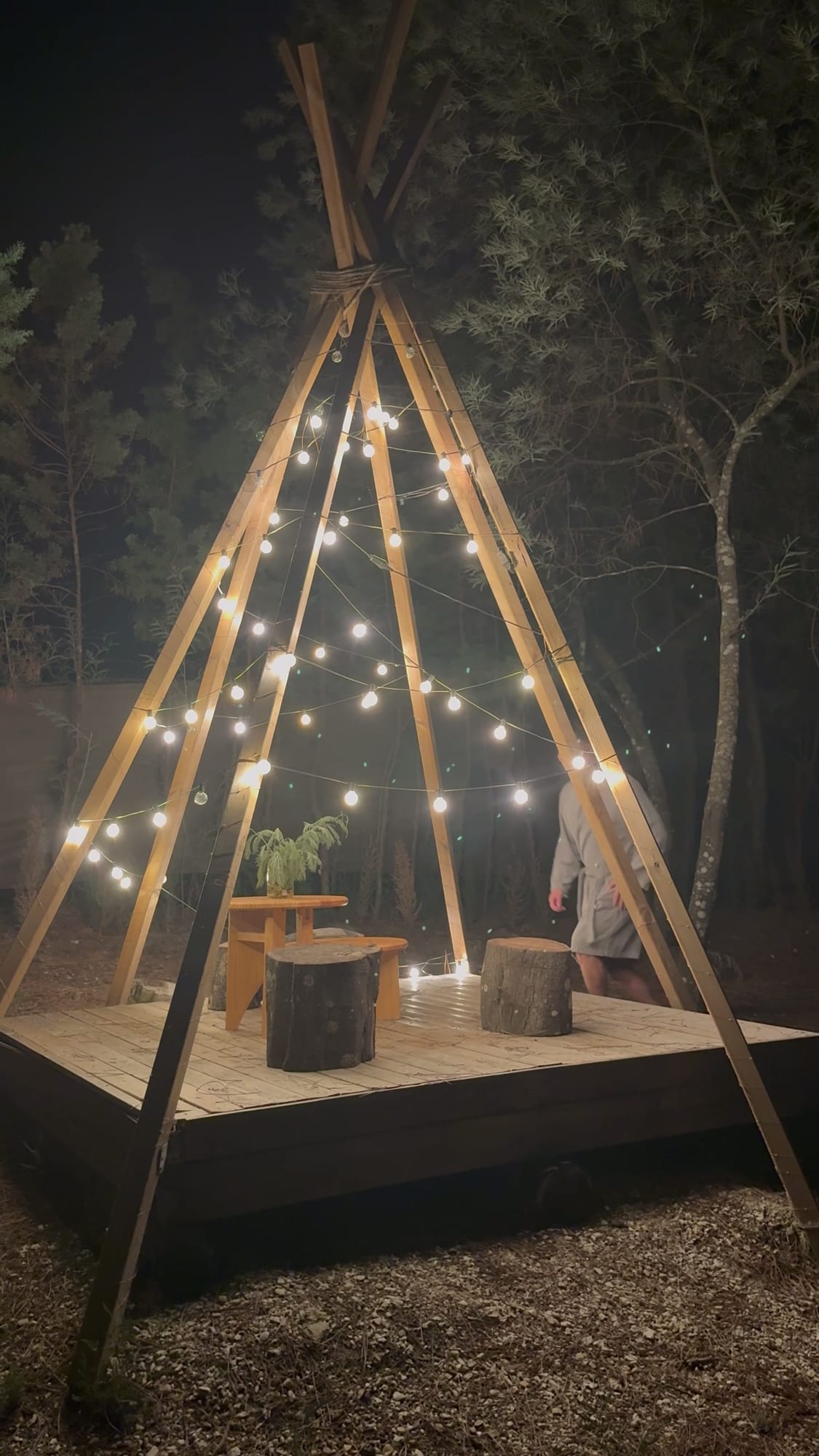 Tarima con estructura de tipi y guirnaldas de luces por la noche en el Glamping The Teepee