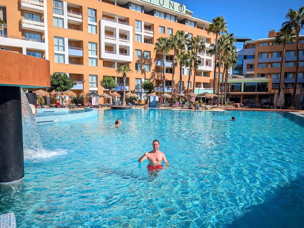 Javier Sobrino en la piscina principal del Hotel Neptuno, con el edificio y el letrero del hotel detrás