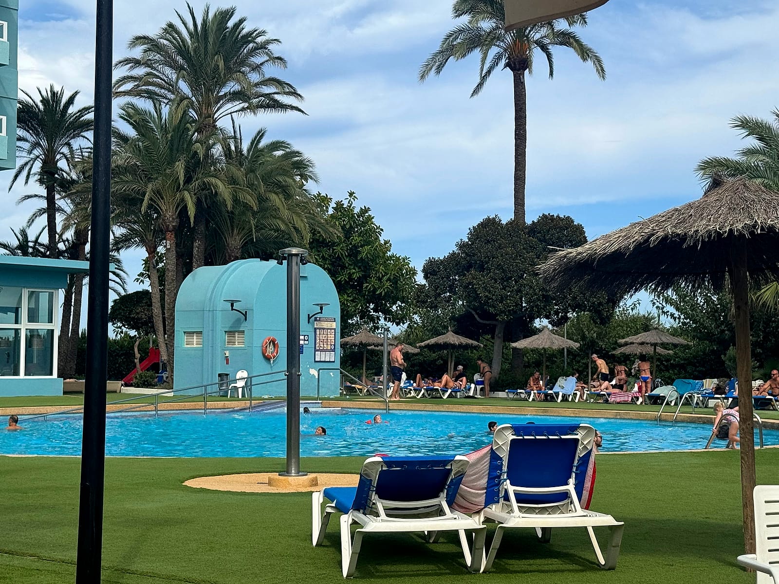 La piscina grande del Hotel Playas de Guardamar, rodeada de césped, palmeras y sombrillas de paja