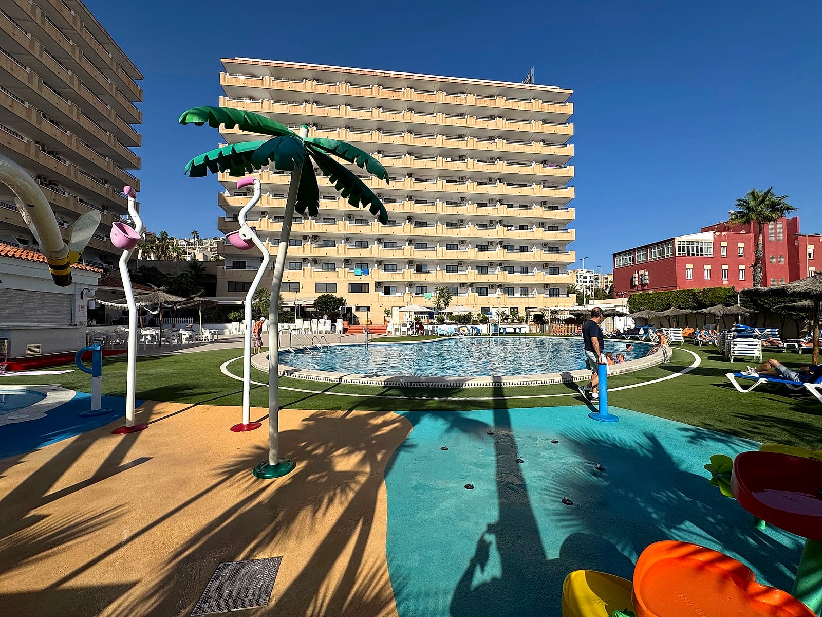 La zona de chapoteo del Hotel Playas de Torrevieja, con flamencos y palmeras de juguete y el edificio detrás