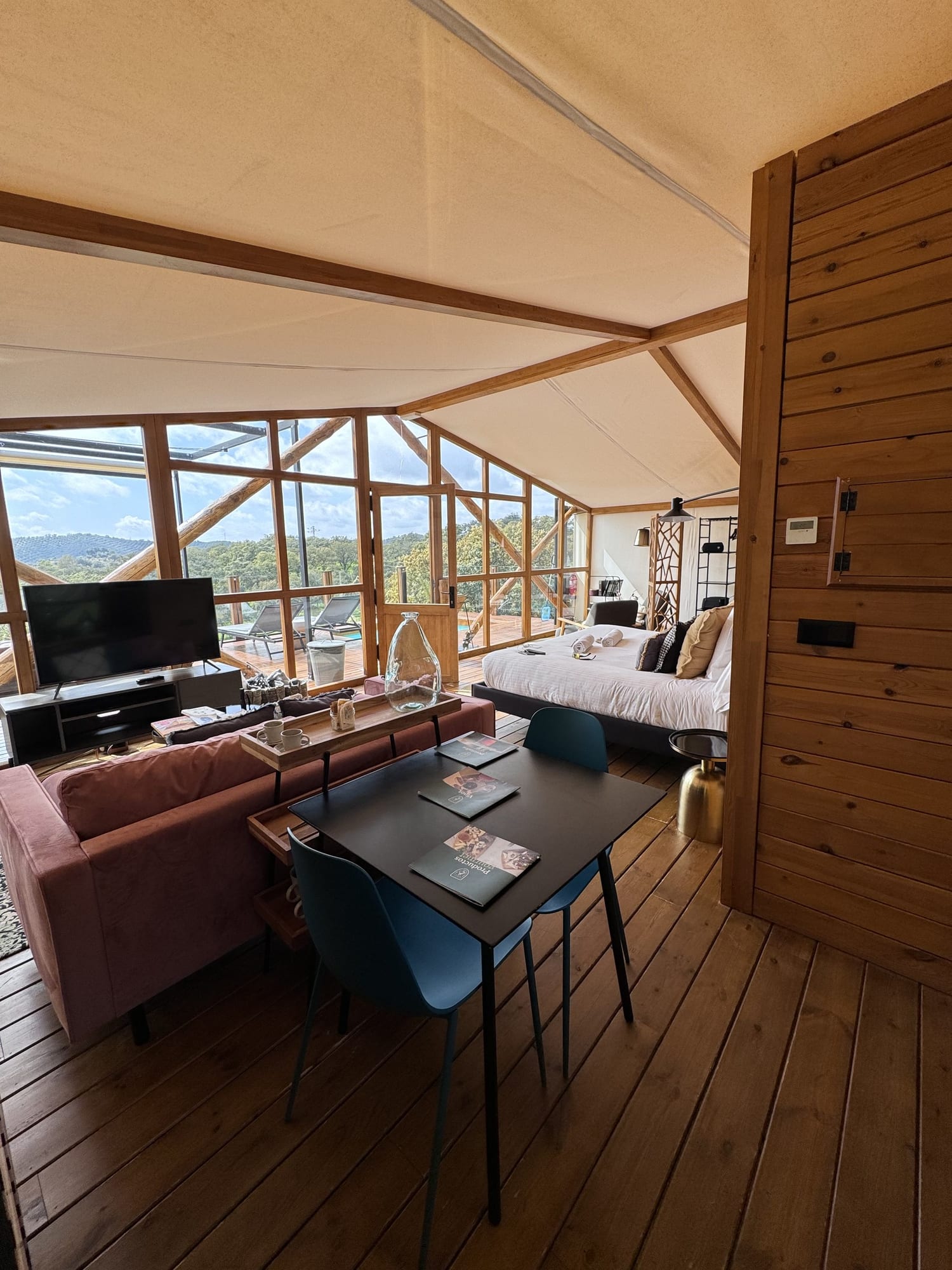 Interior de la cabaña de La Dehesa Experiences con salón, cama y ventanales a la dehesa
