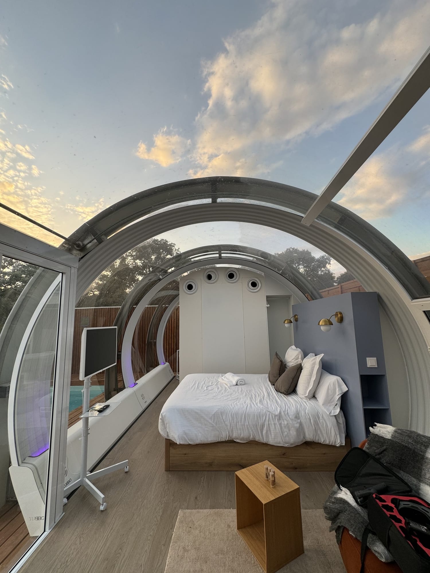 Cápsula con techo de cristal y cama bajo el cielo del atardecer en La Dehesa Experiences