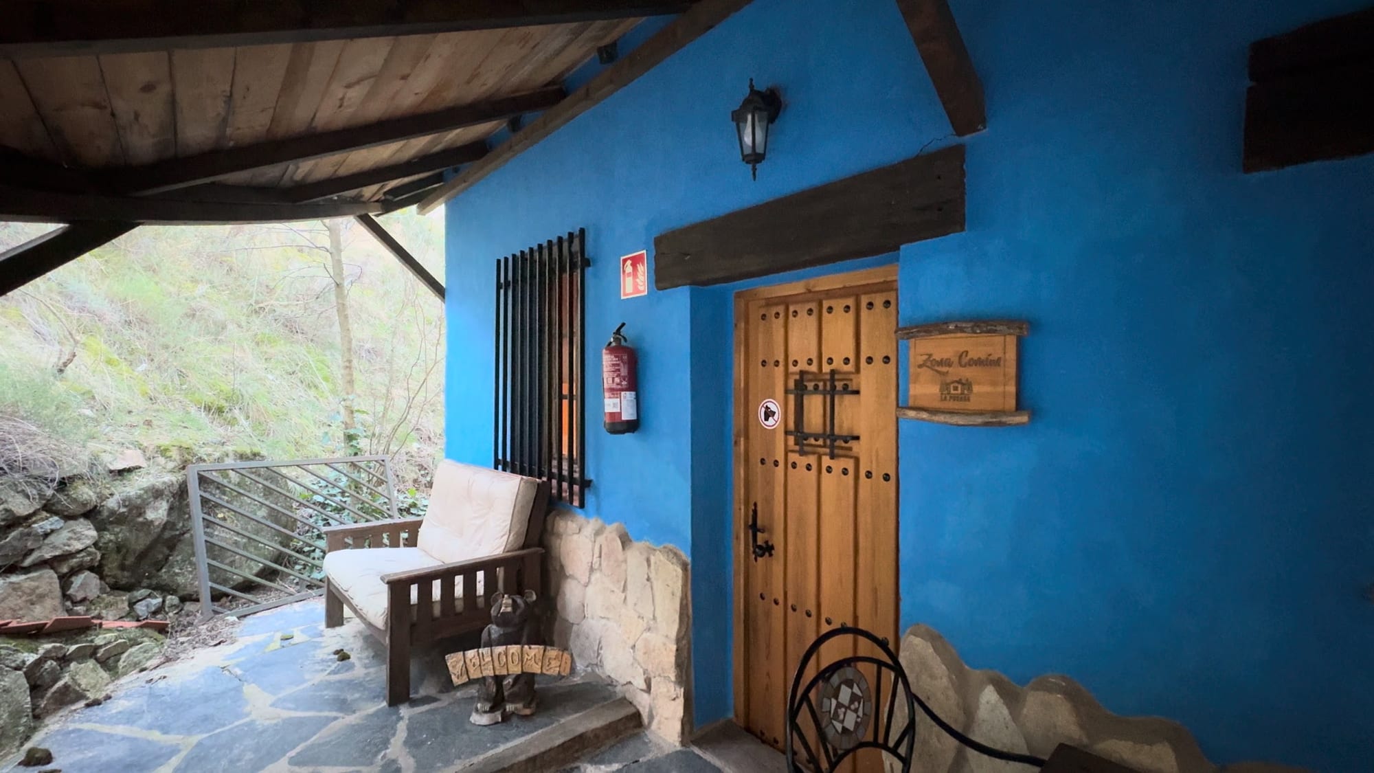 Fachada azul con puerta de madera y banco bajo el porche en La Posada de Cercedilla