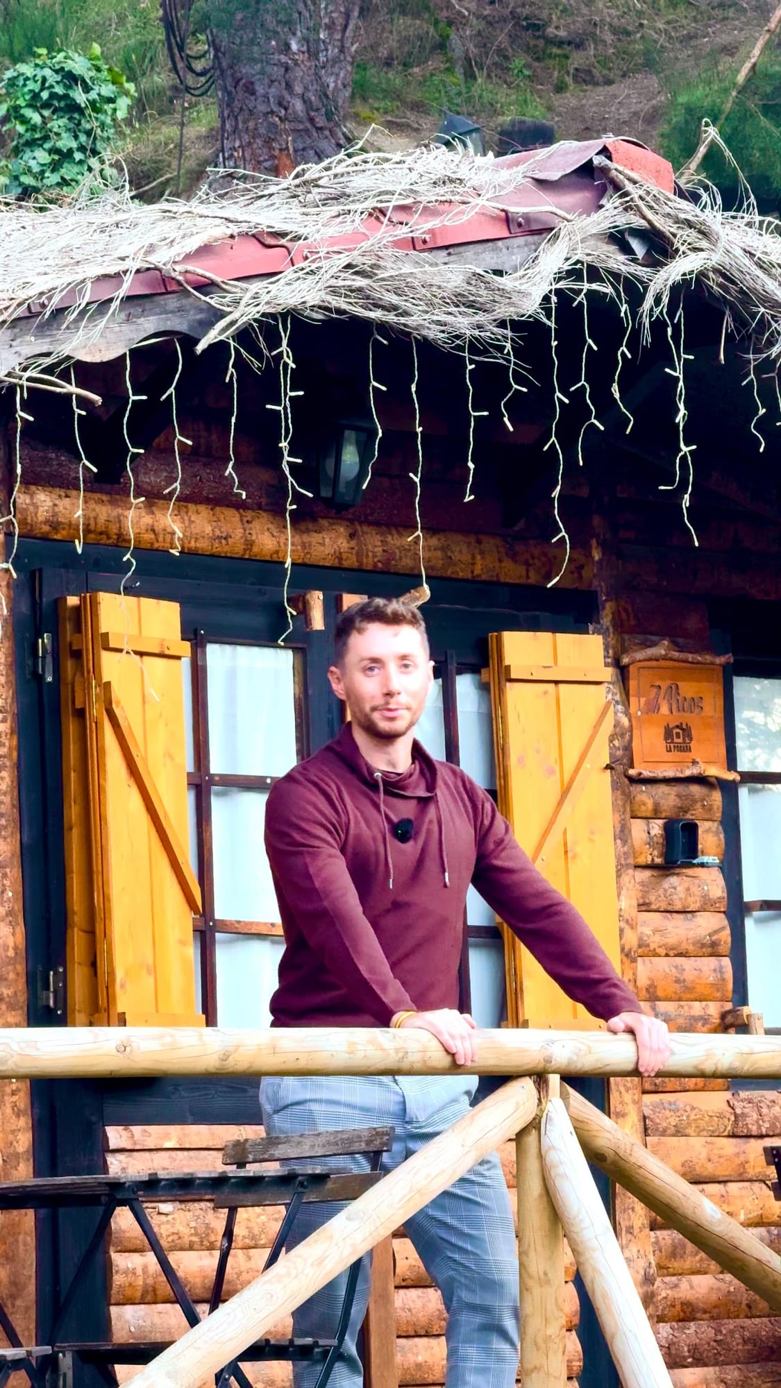 Javier Sobrino en el balcón de una cabaña de troncos con luces colgantes en La Posada de Cercedilla