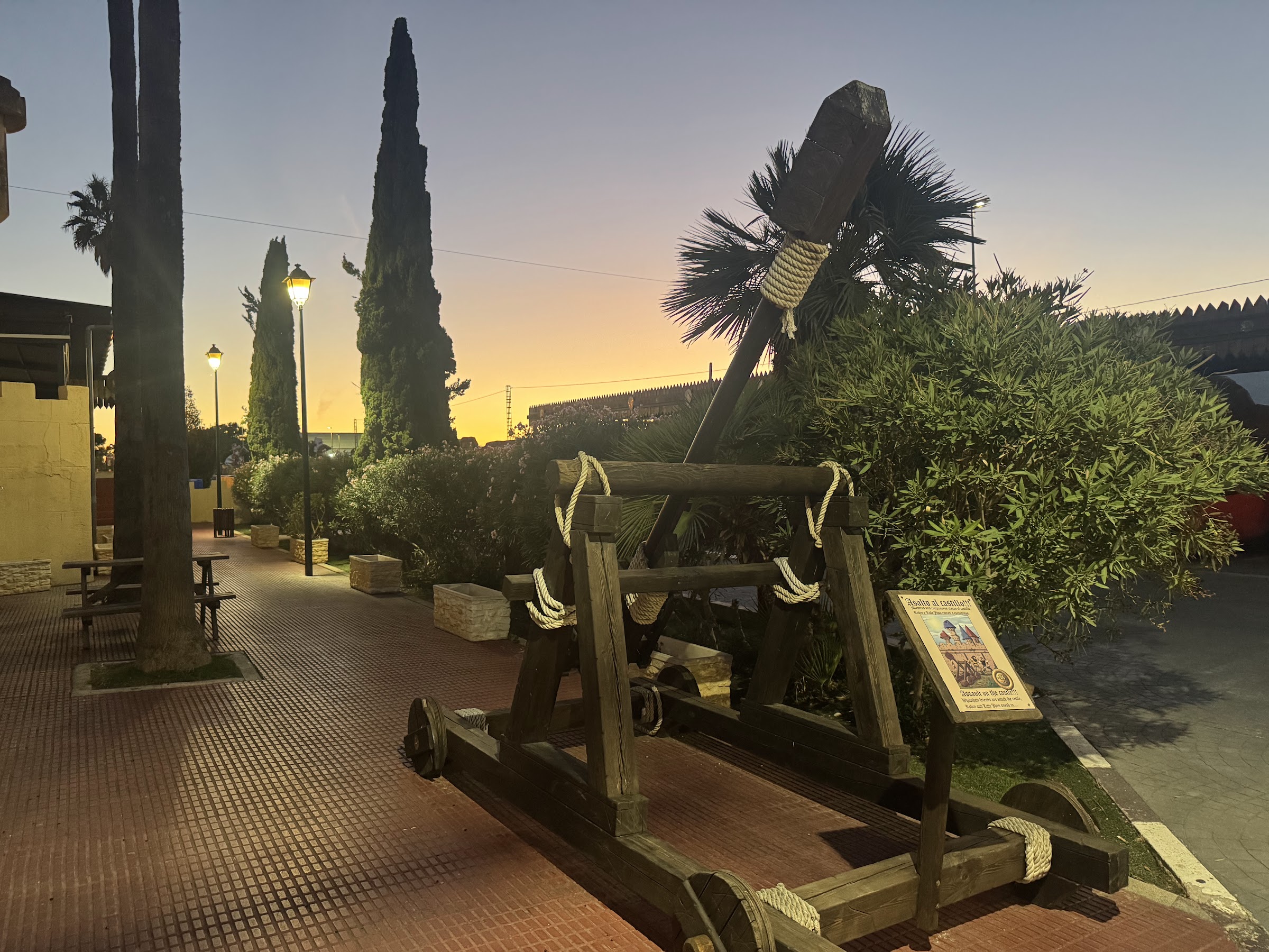 Catapulta de madera junto a un paseo con farolas al atardecer en el Magic Robin Hood Resort