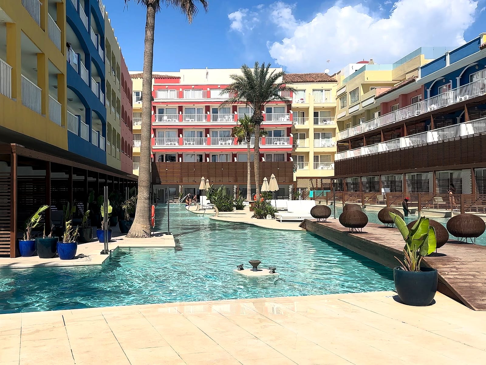 La piscina alargada del Mediterráneo Bay, con pasarelas de madera, palmeras y edificios de colores