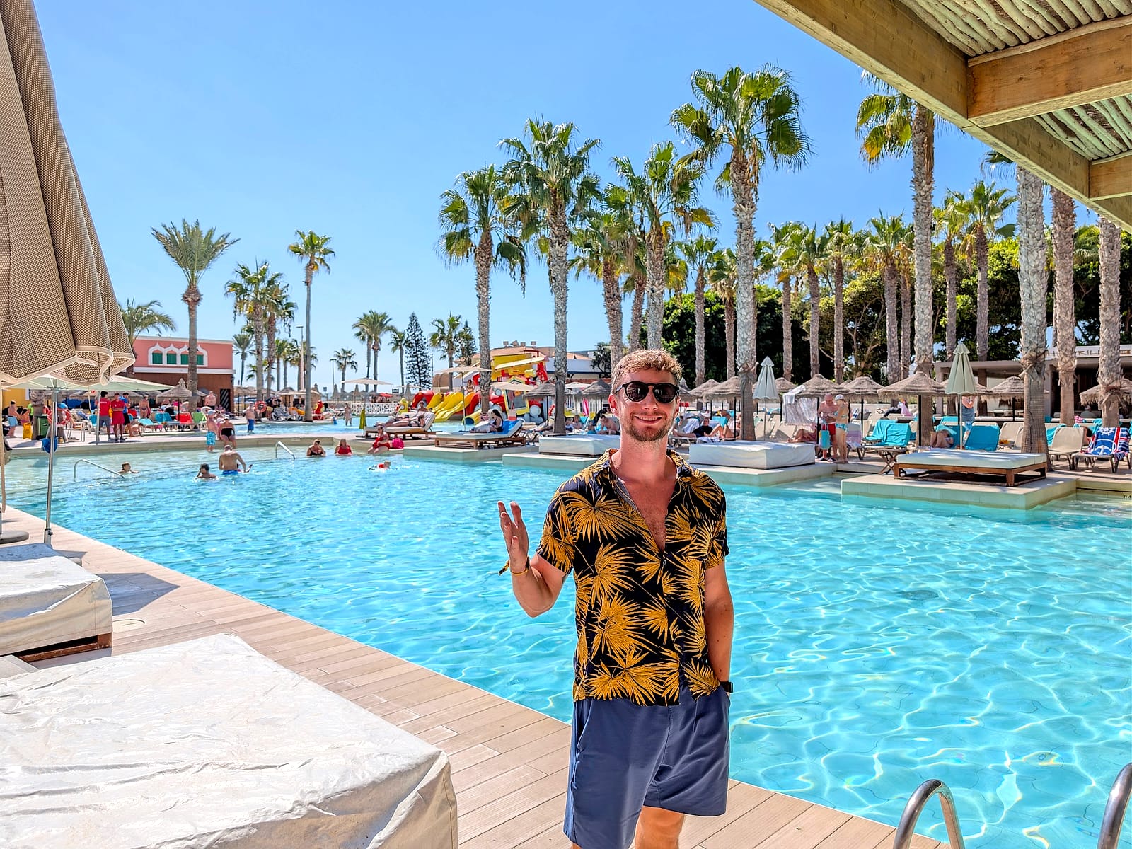 Javier Sobrino saludando junto a la piscina principal del Mediterráneo Bay, con palmeras y camas balinesas