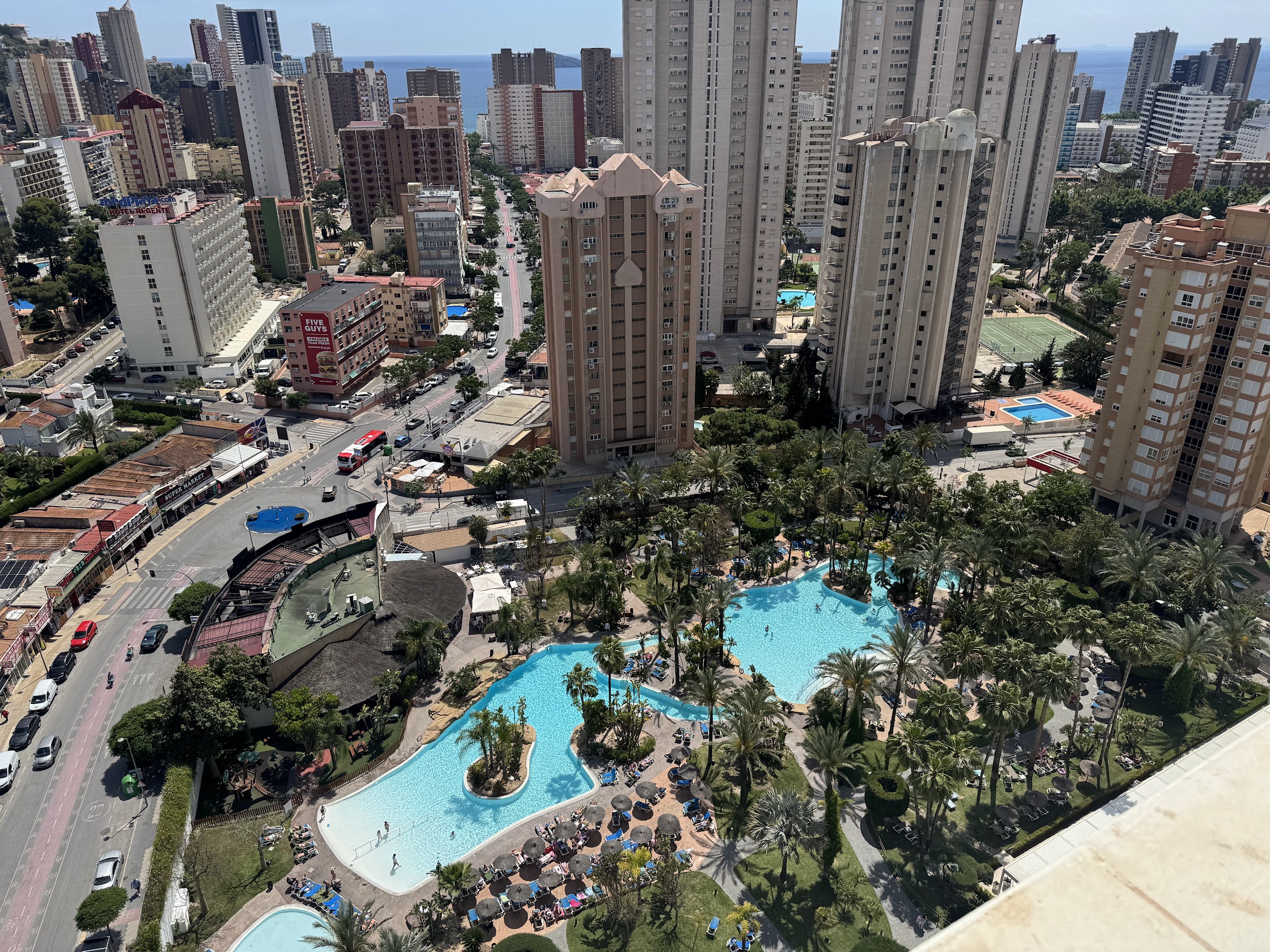 Vista desde lo alto del Meliá Benidorm de sus piscinas entre palmeras y los rascacielos