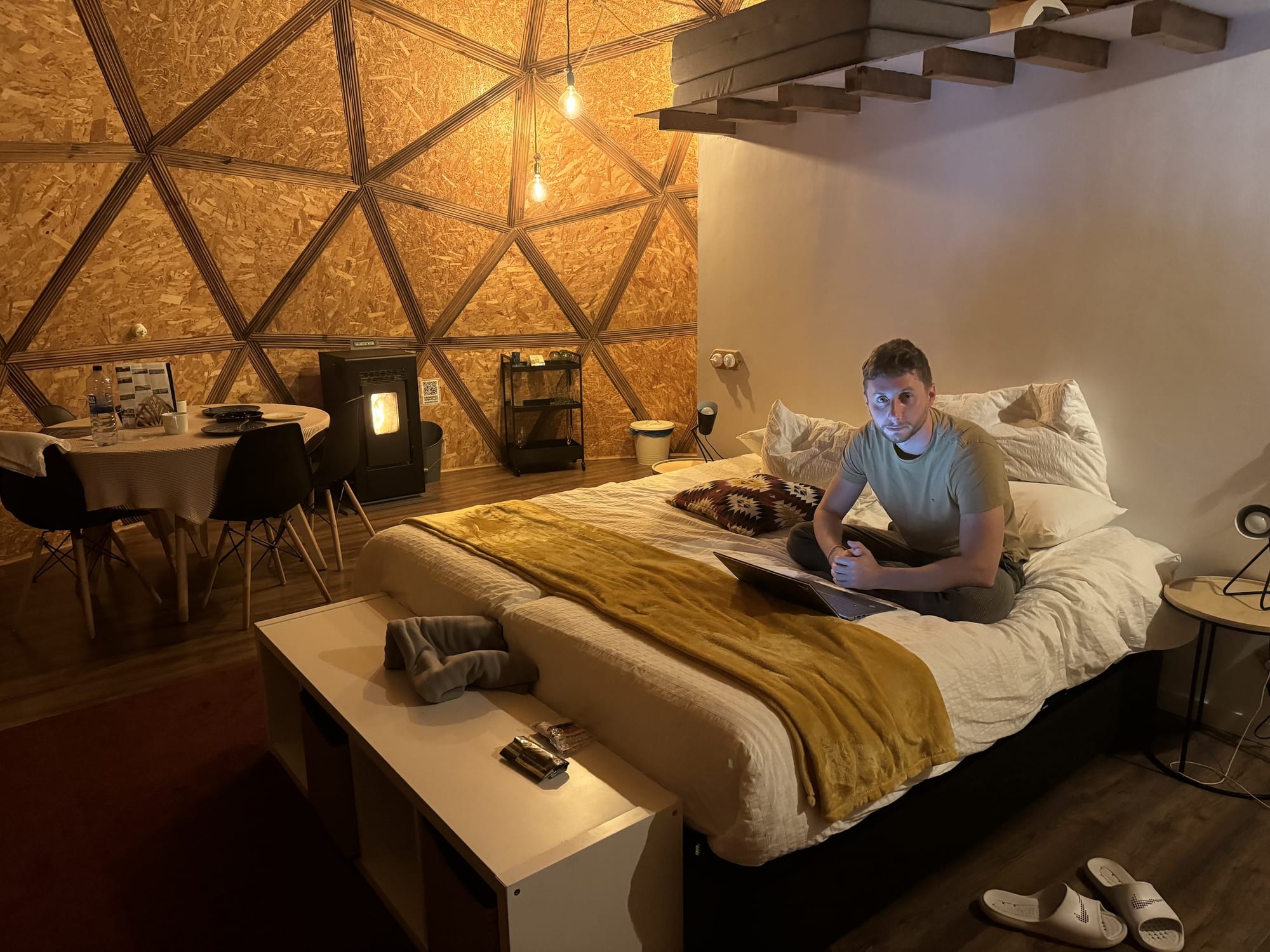 Cama del domo de Miradomos de noche, con la estufa de pellets al fondo