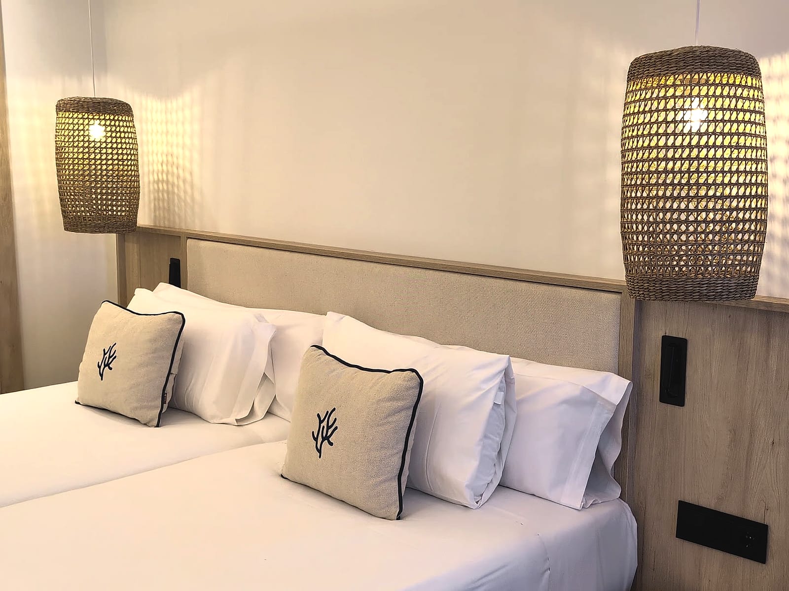 El cabecero de la cama del Pontiana Thalasso, con cojines bordados y lámparas de esparto