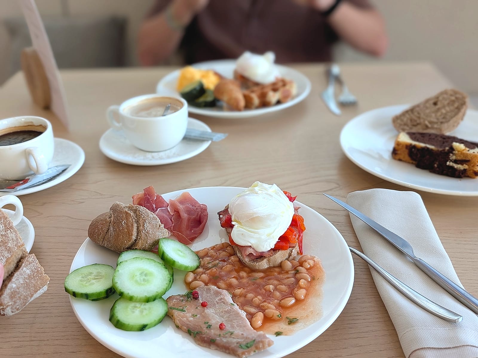 Un plato del desayuno del Pontiana Thalasso, con huevo poché, judías, embutido y pepino, y cafés alrededor