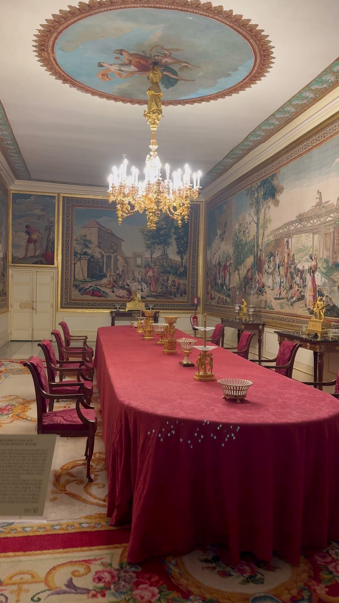 Comedor con mesa de mantel rojo y lámpara de cristal en el Monasterio de El Escorial