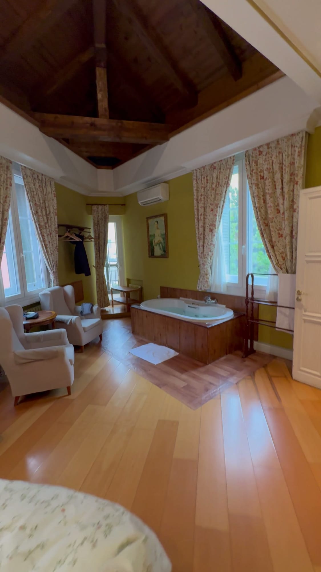 Suite del Hotel Don Jaime con la bañera de hidromasaje junto a la ventana, sillones y techo de madera