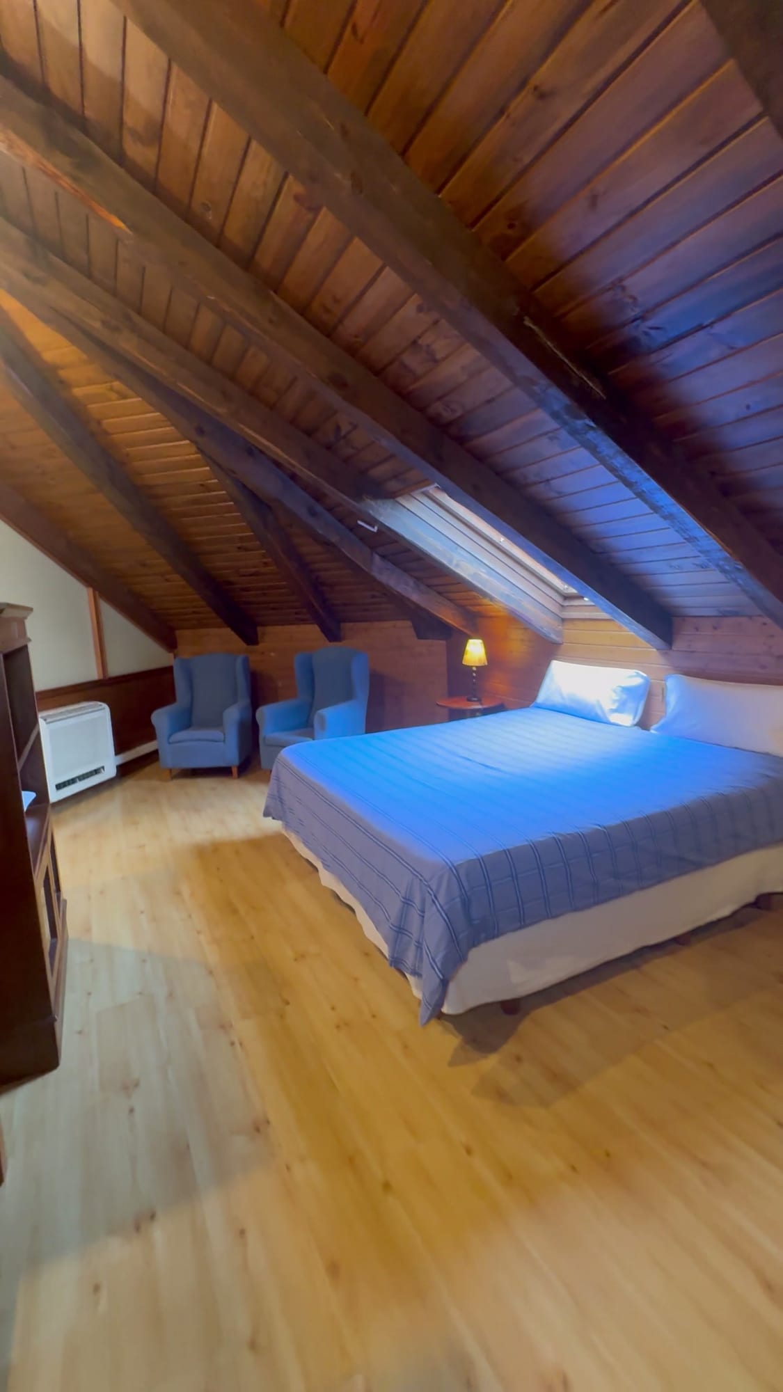 Habitación abuhardillada del Hotel Don Jaime con techo de madera y sillones azules