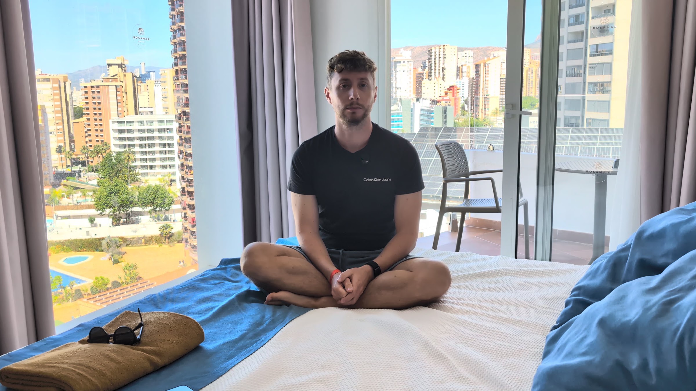 Javier Sobrino sentado en la cama de una habitación del Hotel Rosamar Benidorm con vistas a la ciudad