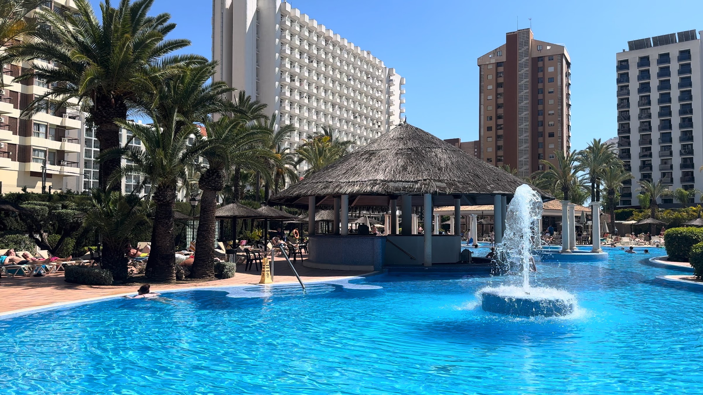 Piscina con fuente y chiringuito de paja entre palmeras en el Sol Pelícanos Ocas