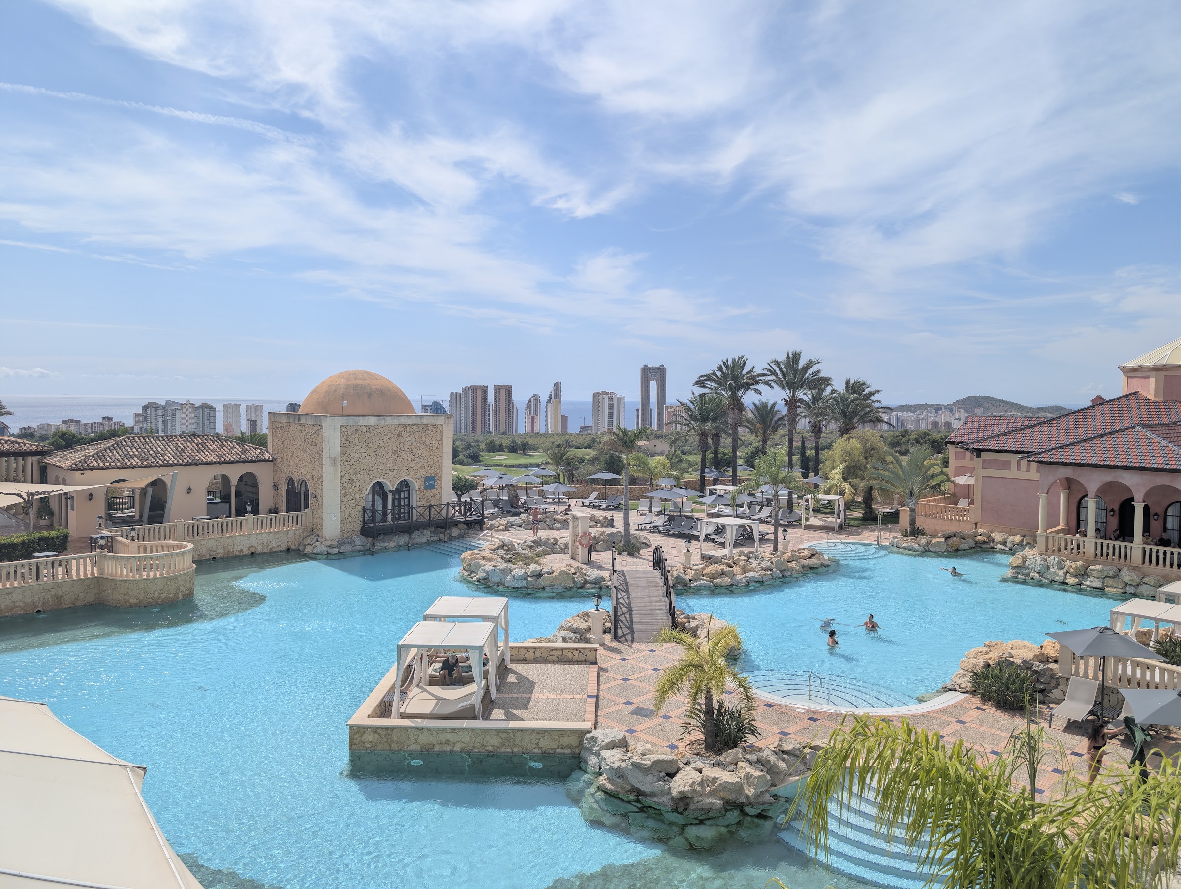 Piscina estilo lago con puentes y camas balinesas del Meliá Villaitana, con Benidorm al fondo