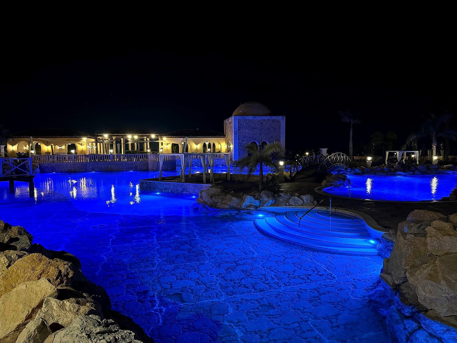 La piscina de The Level iluminada de azul por la noche, con el puente y la cúpula